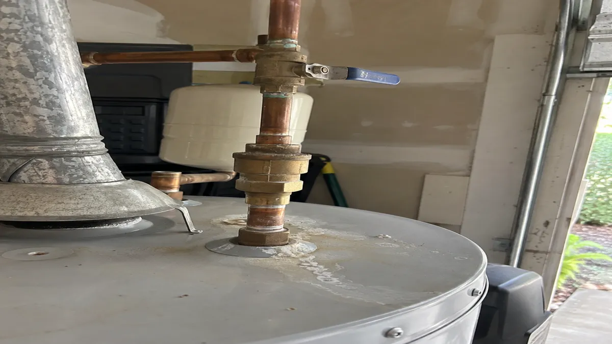 A close view of the cold water supply connection on top of a residential gas water heater, with a shutoff valve and backflow fitting