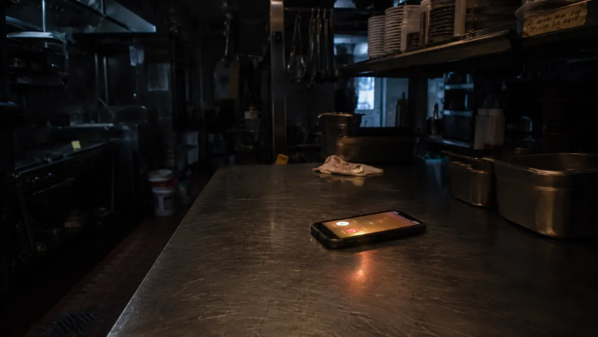 A smartphone glowing with a call on a counter in a dark restaurant kitchen