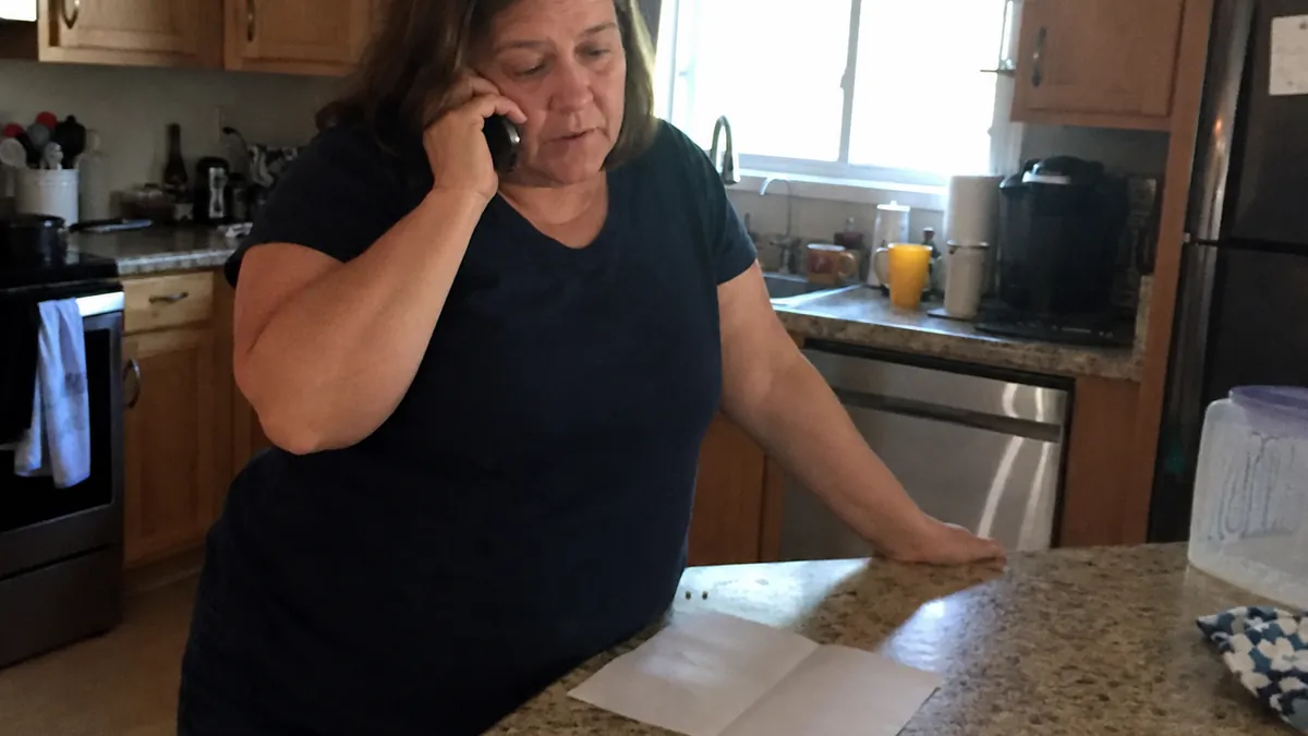 A homeowner standing at a kitchen counter on the phone, with a folded paper estimate and a pen beside her