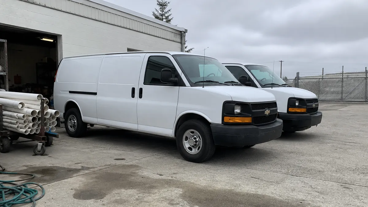 Two plumbing service vans parked outside a small shop's garage