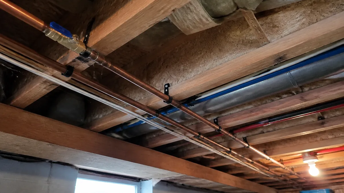 Copper water supply lines running along floor joists in an unfinished basement ceiling